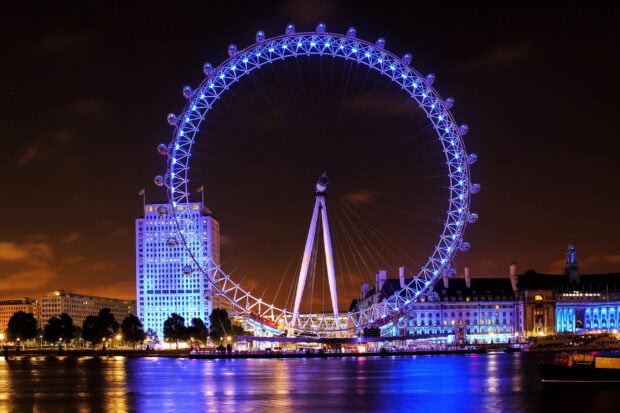 The London Eye shines brightly in blue lights over the river Thames at night, showcasing a stunning cityscape, 2K Desktop Wallpaper