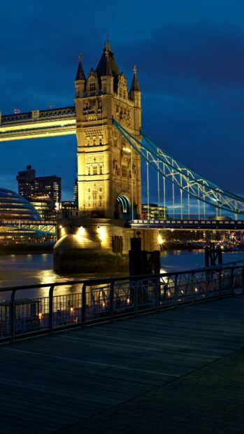 The illuminated Tower Bridge in London is reflected in the river under a dark blue sky as part of United Kingdom Wallpapers, 4K Phone Wallpaper