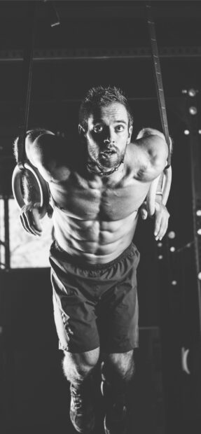 A man is doing an intense Crossfit workout on gymnastic rings with strong focus, 2K Phone Wallpaper