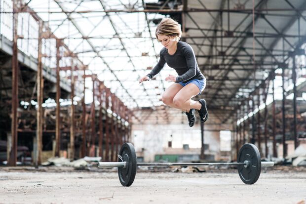 A woman performs a jump over a barbell during Crossfit training in an industrial gym, HD Desktop Wallpaper