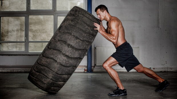 A muscular man is performing a tire flip exercise in a gym setting, HD Desktop Wallpaper