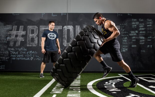 A man performs an intense Crossfit tire flip exercise with a trainer observing, 2K Desktop Wallpaper