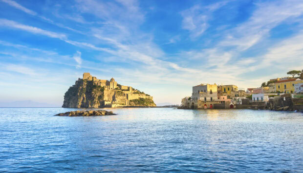 A scenic view of Ischia island with historic castle and coastal buildings under a blue sky