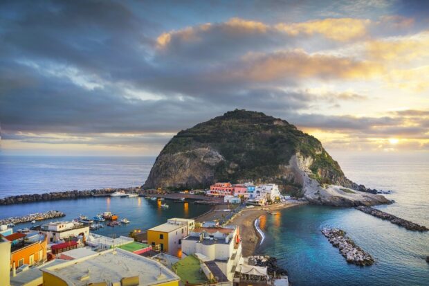 The scenic view of Ischia island with houses and harbor under cloudy sky at sunset