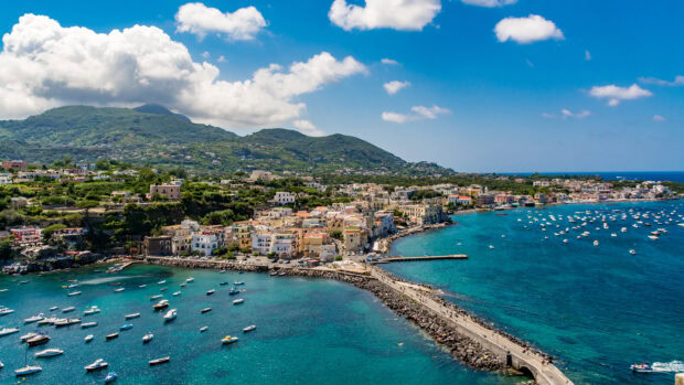 A scenic view of Ischia island with numerous boats and vibrant coastal town under a blue sky