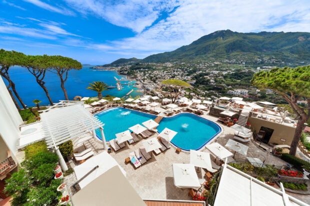 A scenic view of Ischia with a luxury pool and coastal landscape under a bright sky