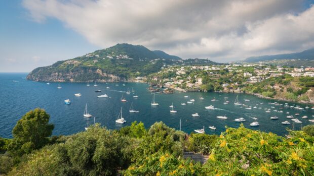 Green hillside of Ischia with boats sailing on the blue sea