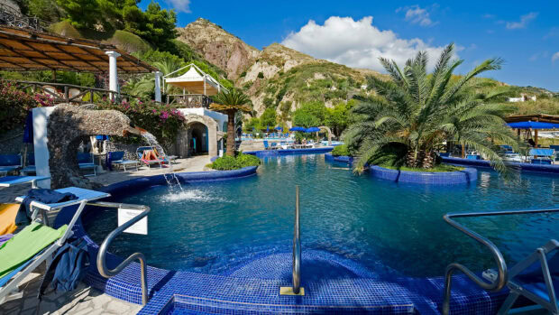 A beautiful pool area with palm trees and mountainous landscape in Ischia region