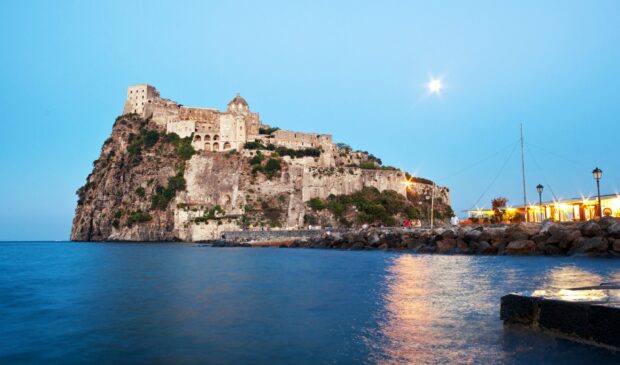 Ancient castle of Ischia island illuminated at dusk over calm sea