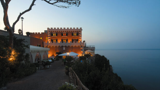 A scenic view of Ischia castle illuminated at dusk overlooking the calm sea