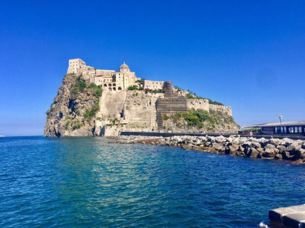 A historic castle on the rocky coast of Ischia under clear blue skies
