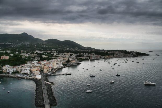 Ischia town coastline with boats and mountains under cloudy sky in HD quality