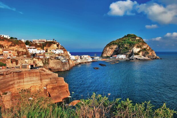 The scenic coastline of Ischia island with rocky cliffs and coastal village under a clear blue sky
