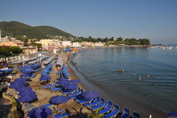 A scenic coastal town with beach umbrellas and hills in Ischia bay