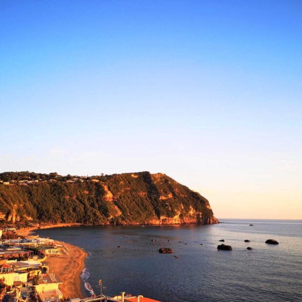 A scenic coastal view of Ischia island with cliffs and calm sea under a clear blue sky