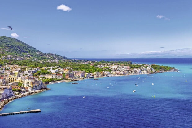 A scenic view of Ischia island coastline with clear blue sea and green hills in the background
