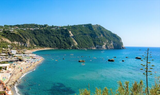 A beautiful coastal view of Ischia with clear blue sea and green cliffs under a bright sky