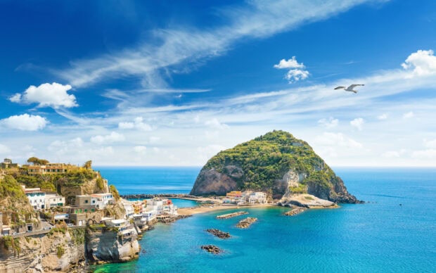 A scenic view of Ischia with rocky cliffs and clear blue sea under a bright sky