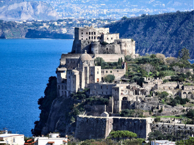 Ancient castle and ruins on the coast of Ischia with blue sea and hillside landscape