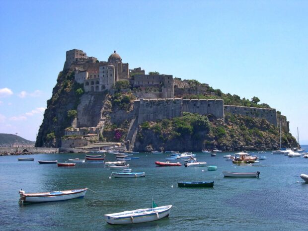 Historic castle on Ischia island with boats floating on the calm sea water