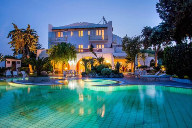 A scenic hotel by the pool surrounded by tropical plants in Ischia at dusk