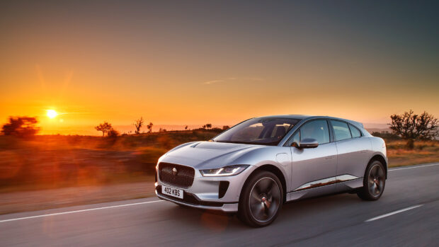 A silver Jaguar I Pace drives on a road during a colorful sunset with trees in the background, HD Desktop Wallpaper