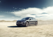 Jaguar I-PACE electric SUV driving on desert terrain under a blue sky.