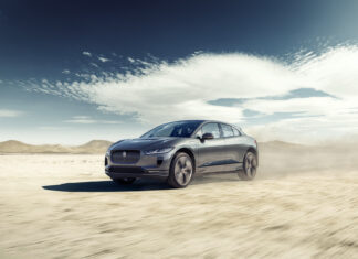 Jaguar I-PACE electric SUV driving on desert terrain under a blue sky.