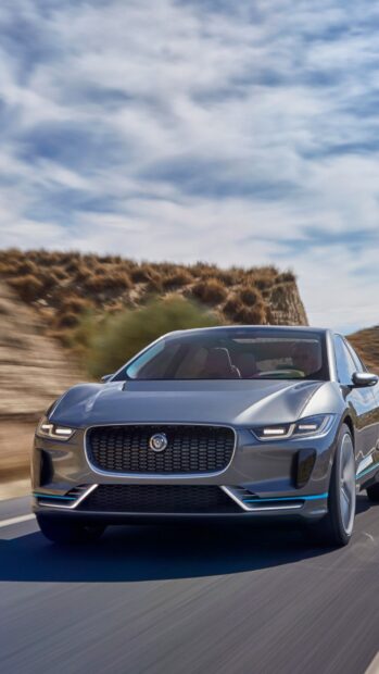 A Jaguar I Pace drives swiftly on a desert road with blue sky in the background, 4K Phone Wallpaper