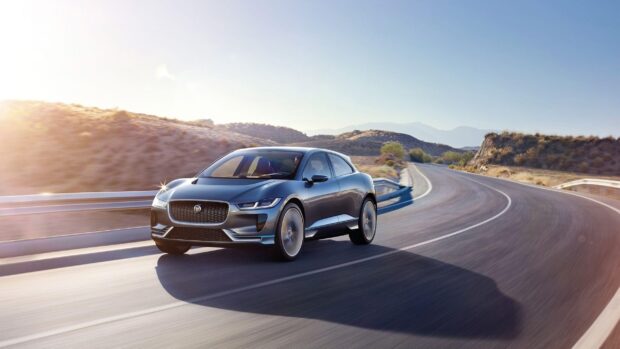 A Jaguar I Pace driving swiftly along a winding mountain road under clear skies, 2K Desktop Wallpaper