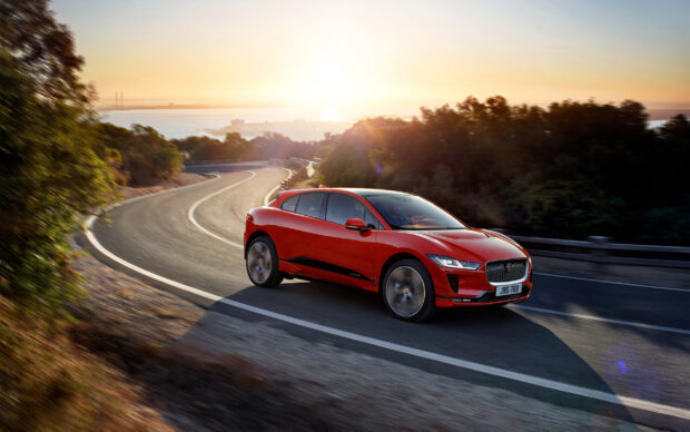 A red Jaguar I Pace car is driving along a winding road during sunset, 2K Desktop Wallpaper