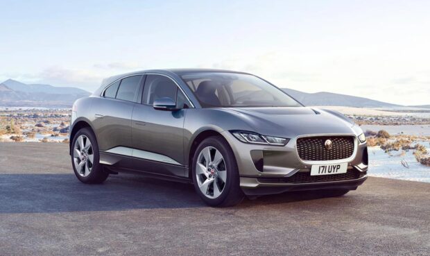 A silver Jaguar I Pace electric SUV is parked on a scenic road with mountains in the background, HD Desktop Wallpaper