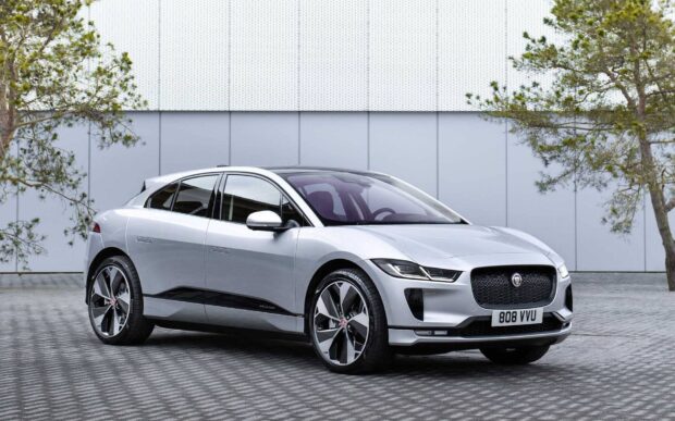 A silver Jaguar I Pace electric car parked in front of a wall with trees on each side, HD Desktop Wallpaper