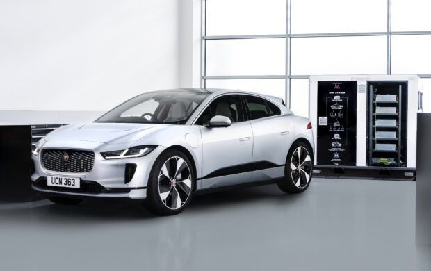 A silver Jaguar I Pace is parked in a bright garage near battery storage equipment, HD Desktop Wallpaper