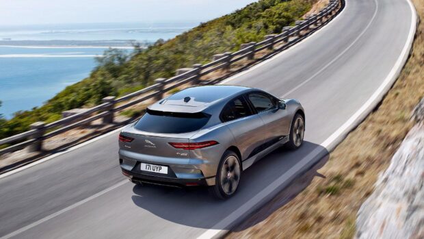 A Jaguar I Pace drives along a winding coastal road with the ocean visible in the background, HD Desktop Wallpaper