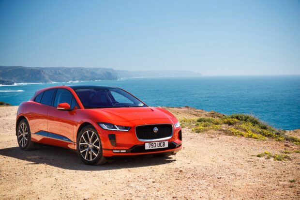 A red Jaguar I Pace is parked on a coastal cliff with a clear blue sky and ocean in the background, HD Desktop Wallpaper