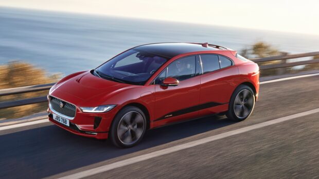 A red Jaguar I Pace electric car is driving on a coastal road with the ocean in the background, 2K Desktop Wallpaper