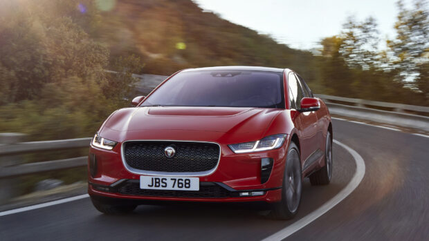 A red Jaguar I Pace is driving on a curvy mountain road surrounded by trees and barriers, 2K Desktop Wallpaper
