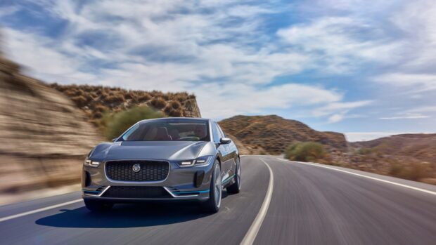 A Jaguar I Pace drives on a winding desert road under a blue sky, 4K Desktop Wallpaper