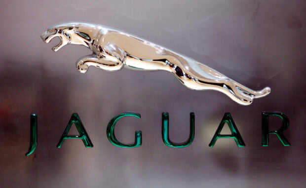A shiny metal jaguar emblem representing the Jaguar brand with bold letters Jaguar on a smooth surface
