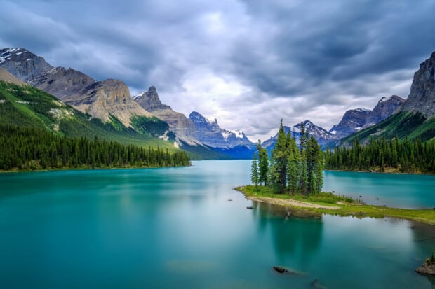 A serene view of Jasper National Park with turquoise lake and mountain peaks under cloudy sky