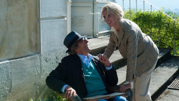 A man wearing a hat smiles while sitting in a chair with a woman leaning over him in a garden, 4K Desktop Wallpaper