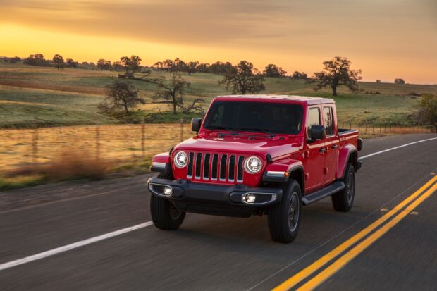 Red Jeep Gladiator driving on a countryside road during sunset