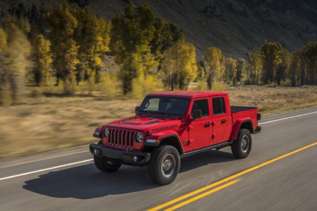 Red Jeep Gladiator driving on a highway with autumn trees in the background