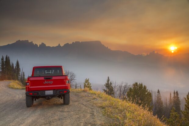 Red Jeep Gladiator parked on mountain road at sunset with scenic landscape background