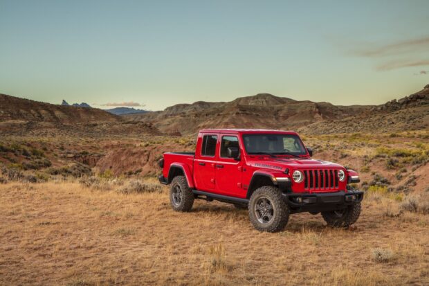 Red Jeep Gladiator truck parked on dry grassland in rugged mountain terrain