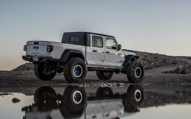 White Jeep Gladiator truck parked near a rocky water puddle reflecting its image