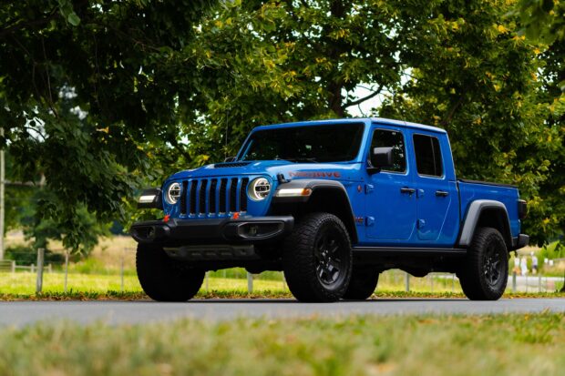 Blue Jeep Gladiator parked on a road surrounded by green trees and grass