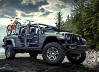 A Jeep Gladiator carrying mountain bikes parked on rocky terrain near a forest and lake