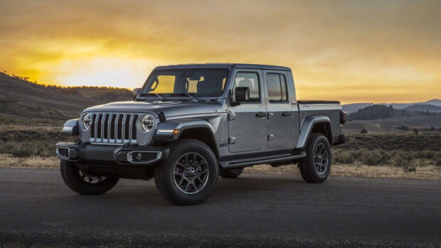 A gray Jeep Gladiator parked on a road with hills and a sunset sky in the background